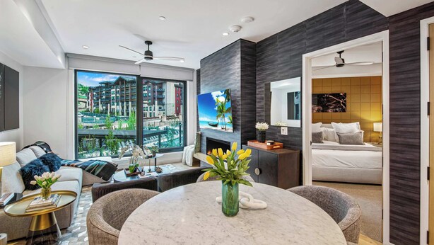 A modern hotel room with a large window, a fireplace, a dining area, and a separate bedroom. - Modern 2 bedroom 2 bathroom Ski In&Ski Out 07 (Snowmass Village)