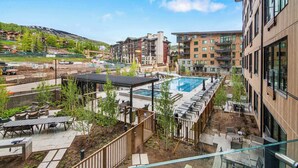 A modern residential complex with a swimming pool, outdoor seating, and a view of a hilly landscape. - Modern 2 bedroom 2 bathroom Ski In&Ski Out 07 (Snowmass Village)