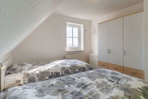 A bedroom with two beds, a window, a radiator, and a wardrobe. - Ferienwohnung in Westerdeichstrich (Westerdeichstrich)