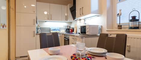 A modern kitchen with white cabinets, a microwave, and a stove. There is a dining table set with plates, a glass, and cutlery.