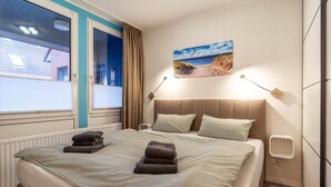 A hotel room with a bed, a painting of a beach scene, and a window with curtains. - Ferienwohnung in Büsum (Büsum)