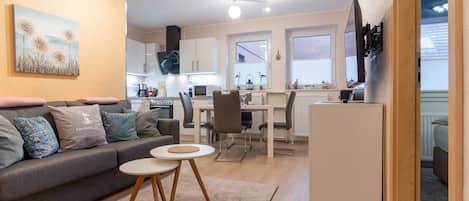 A modern living room with a sofa, a small round table, and a kitchen area with cabinets and a dining table.