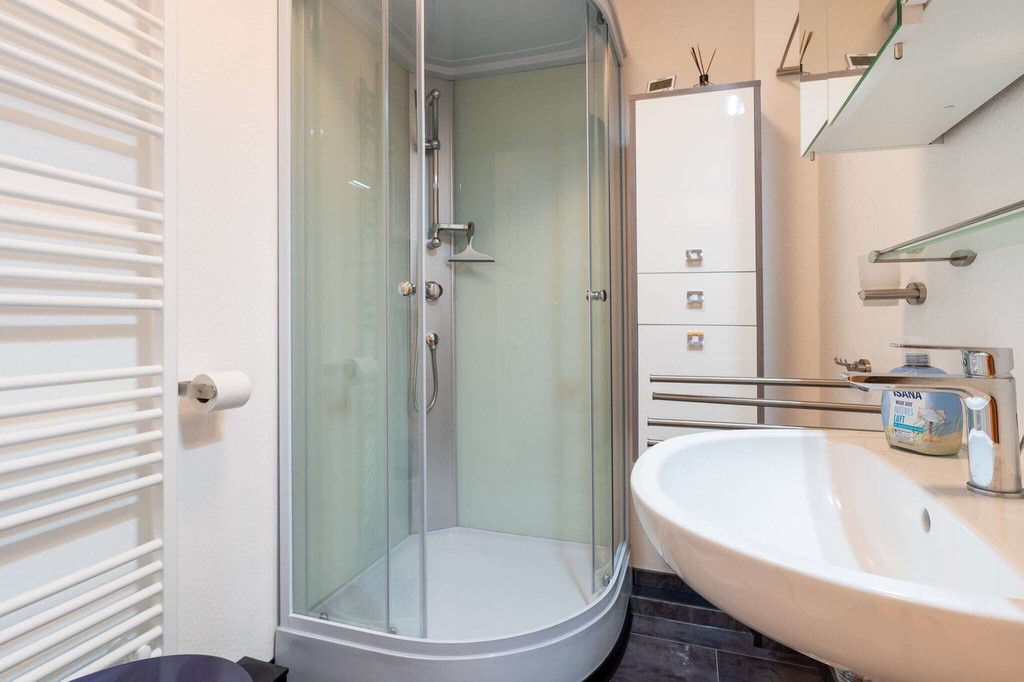Ein modernes Badezimmer mit einer in Glas abgeschlossenen Dusche, einem weißen Waschbecken und einem Schrank mit Schubladen.