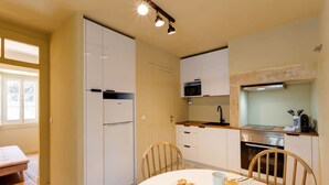 Uma cozinha compacta com armários brancos, micro-ondas e pia. Há uma mesa de jantar com pratos e um copo de suco.