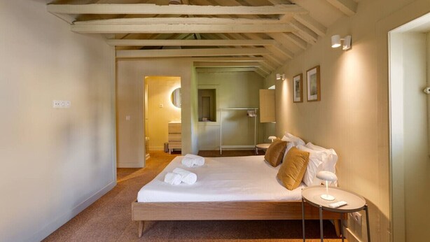 Quarto com cama de madeira, mesa de cabeceira redonda e um espelho na parede.