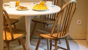 Uma área de jantar com uma mesa redonda, quatro cadeiras de madeira e um prato de comida acompanhado de bebidas.