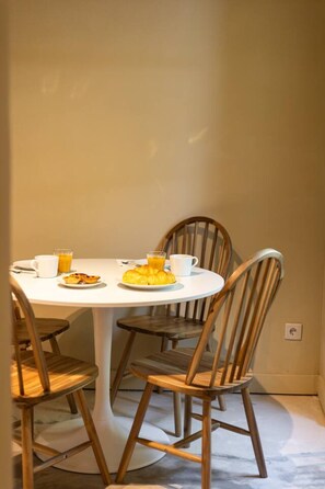 Un comedor con una mesa redonda, cuatro sillas de madera y un plato de comida con bebidas.