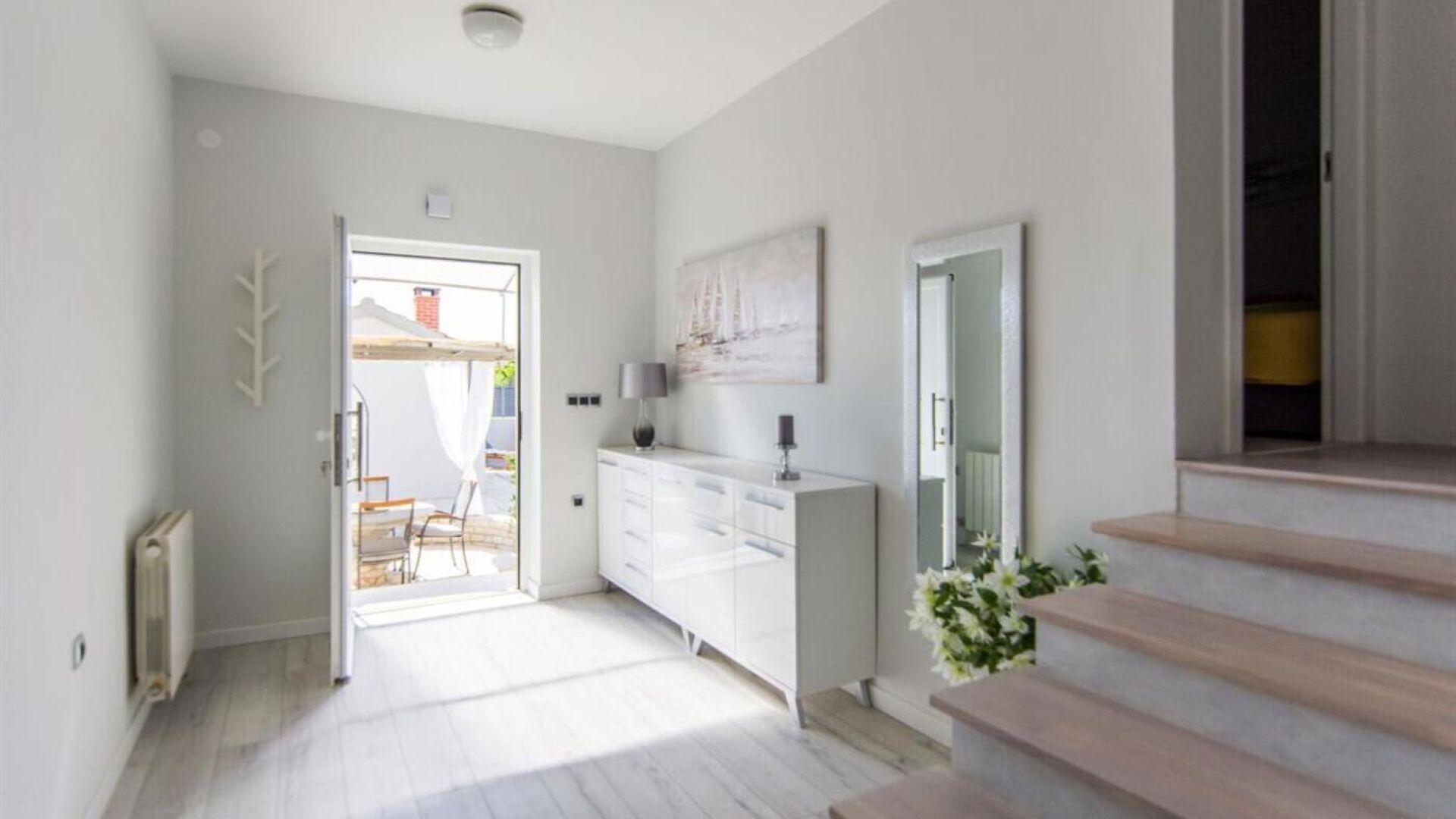 Un couloir lumineux avec un escalier blanc, une armoire blanche et une porte donnant sur un espace extérieur.