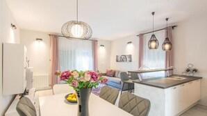 Eine moderne Küche mit Essbereich, ausgestattet mit einer zentralen Kochinsel, Pendelleuchten und einem Blumenstrauß auf dem Tisch.