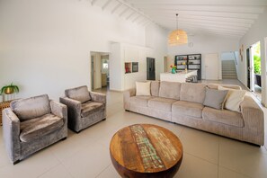 Ein modernes Wohnzimmer mit einer Couch, zwei Sesseln, einem Couchtisch und einer Küche im Hintergrund.
