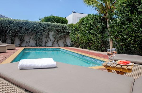 A swimming pool with lounge chairs and a table with glasses and watermelon.