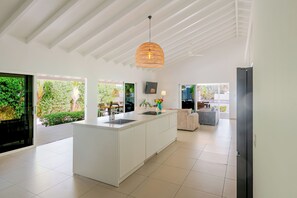 Una cocina moderna con una isla central, ventanas amplias y un techo con vigas blancas.