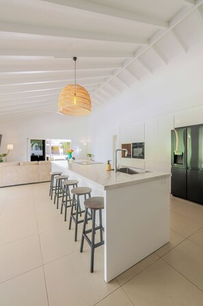A modern kitchen with a central island, bar stools, a hanging light fixture, and a built-in refrigerator.