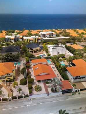 Vista aérea de una zona residencial costera con casas, piscina y vistas al mar.