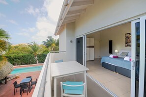 A hotel room with a balcony, a pool, and a view of palm trees.