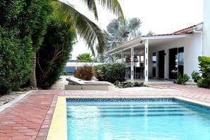 A swimming pool with a tiled edge, surrounded by a brick pathway and lush greenery. - Tropical villa with a private pool near the beach (Jan Thiel)