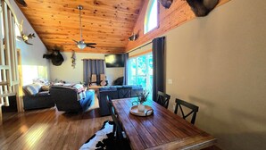 L'interno accogliente di un rifugio, con soffitto in legno, tavolo da pranzo, divano e un'ampia finestra.
