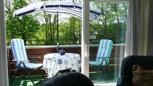A sunlit patio with two striped chairs, a table with a patterned tablecloth, and a large umbrella.