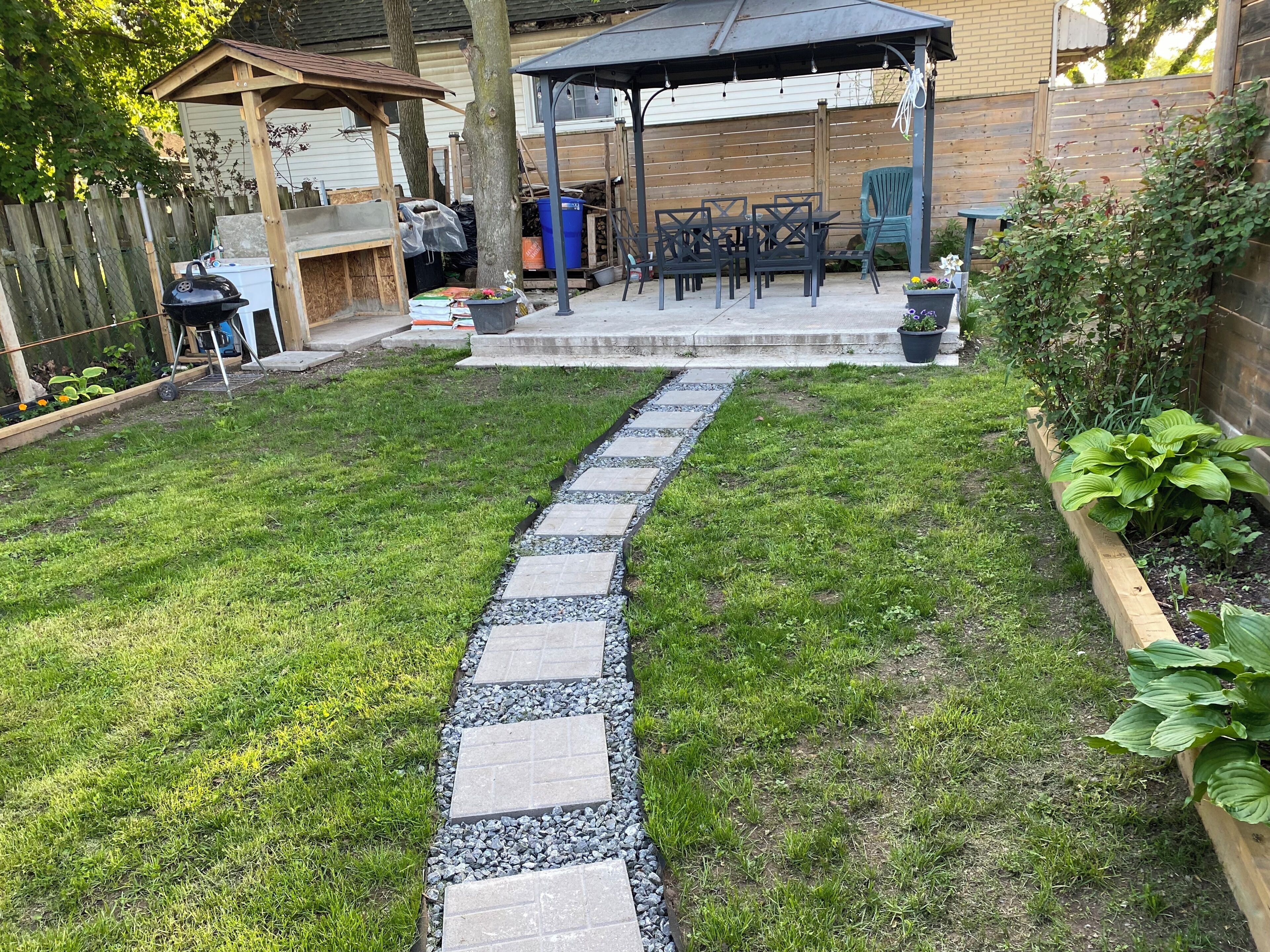 A backyard with a stone pathway leading to a patio area with outdoor furniture.
