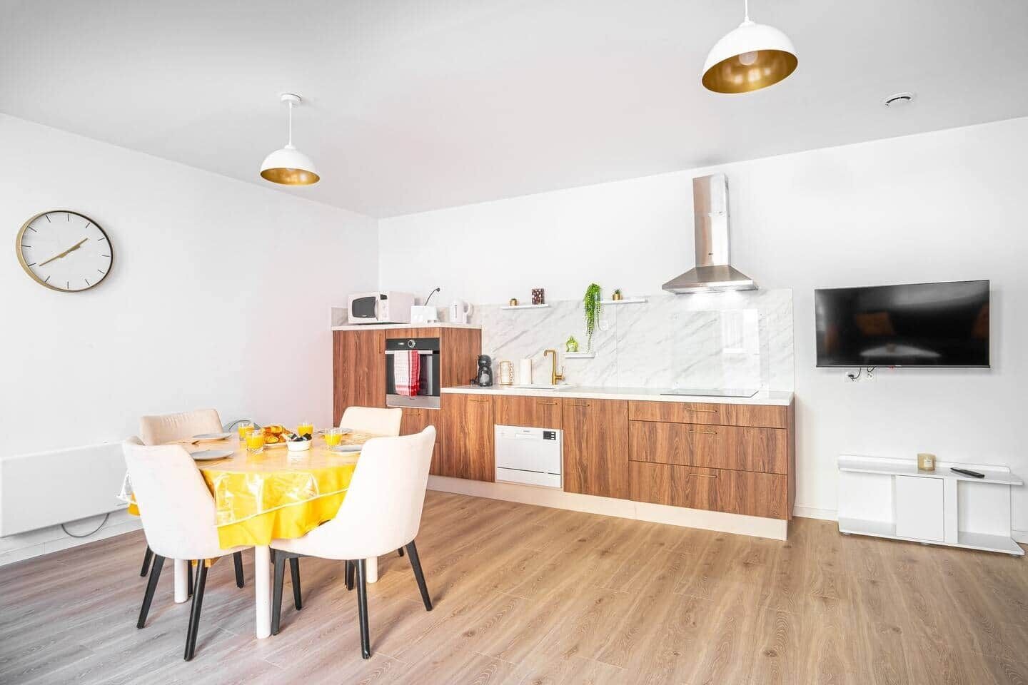A modern kitchen with a dining area, wooden cabinets, a built-in oven, and a TV mounted on the wall.