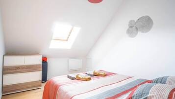 A bedroom with a sloped ceiling, a bed with striped bedding, a bedside table, a radiator, and a window.