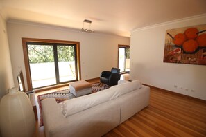 Ein Wohnzimmer mit einer Couch, einem Sessel, einem großen Fenster und einem Gemälde an der Wand.