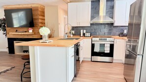 A modern kitchen with a central island, built-in oven, stainless steel appliances, and a stone backsplash. - Modern Oasis with Pool + Putting Green (Pinellas Park)