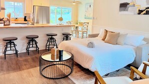 A modern bedroom with a large bed, a round coffee table, and a kitchen area with bar stools. - Modern Oasis with Pool + Putting Green (Pinellas Park)