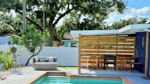 A swimming pool with a wooden deck area, outdoor furniture, and a pergola structure. - Modern Oasis with Pool + Putting Green (Pinellas Park)
