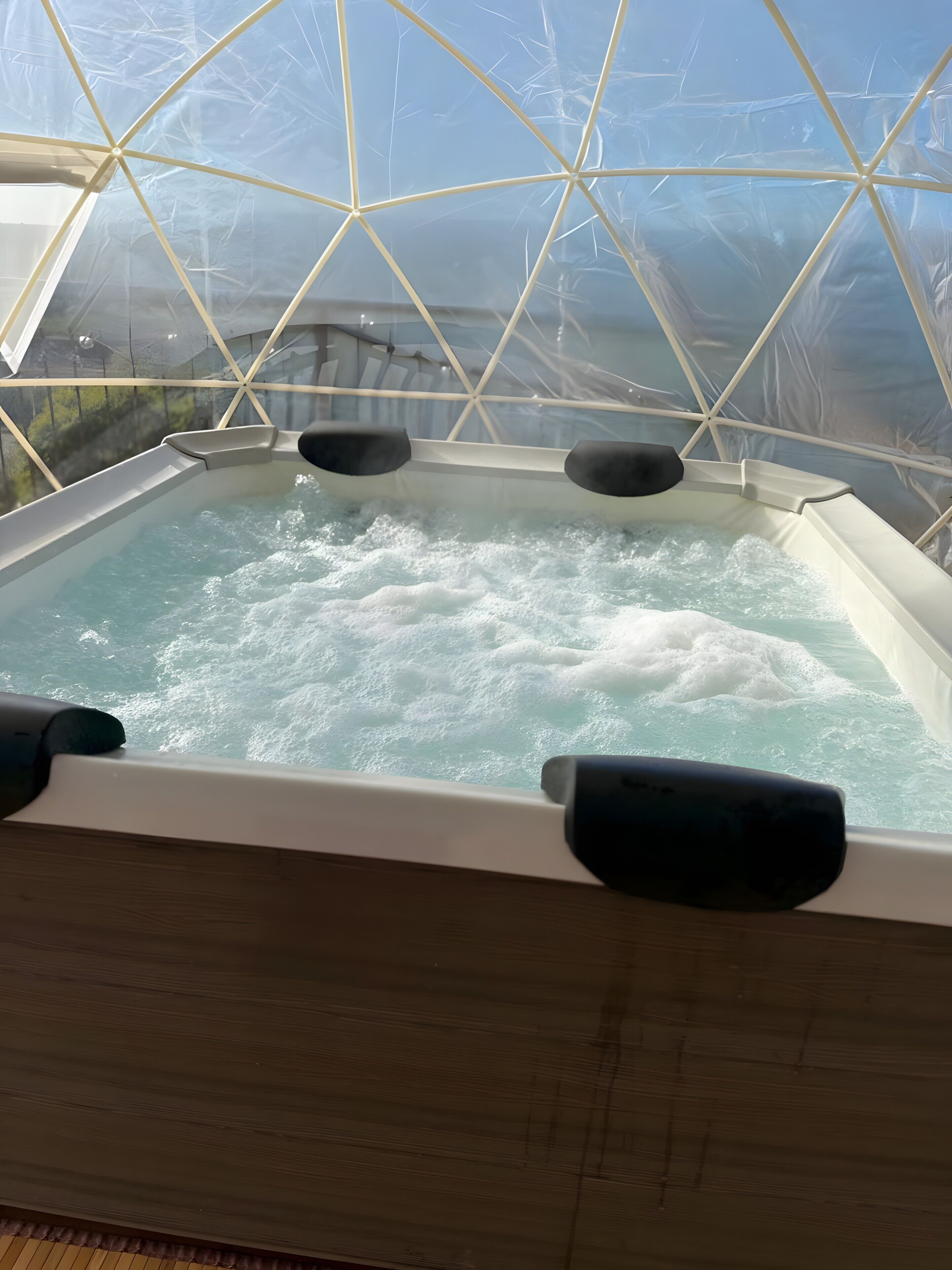 A hot tub with a geometric glass enclosure, water jets, and a view of the outdoors.