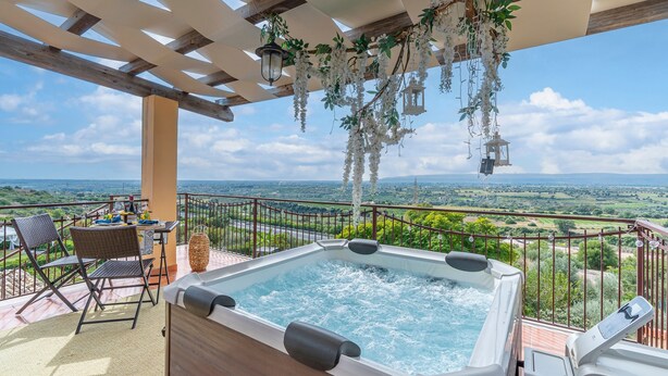 Een bubbelbad met panoramisch uitzicht, een tafel met stoelen en hangplanten.