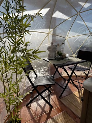 Une serre avec une table et des chaises, une lampe et une plante en pot.