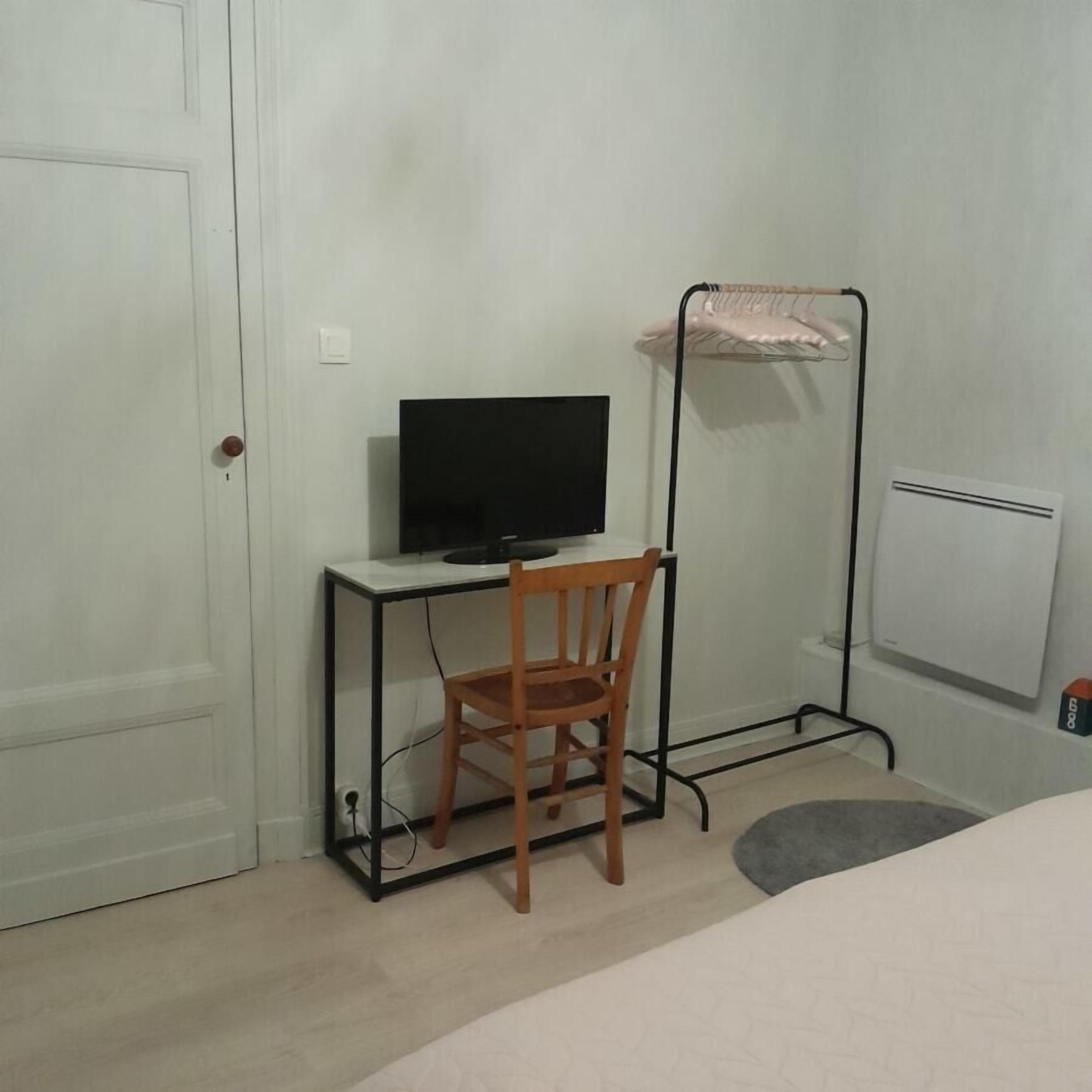 A small room with a desk, chair, TV, radiator, and a door.