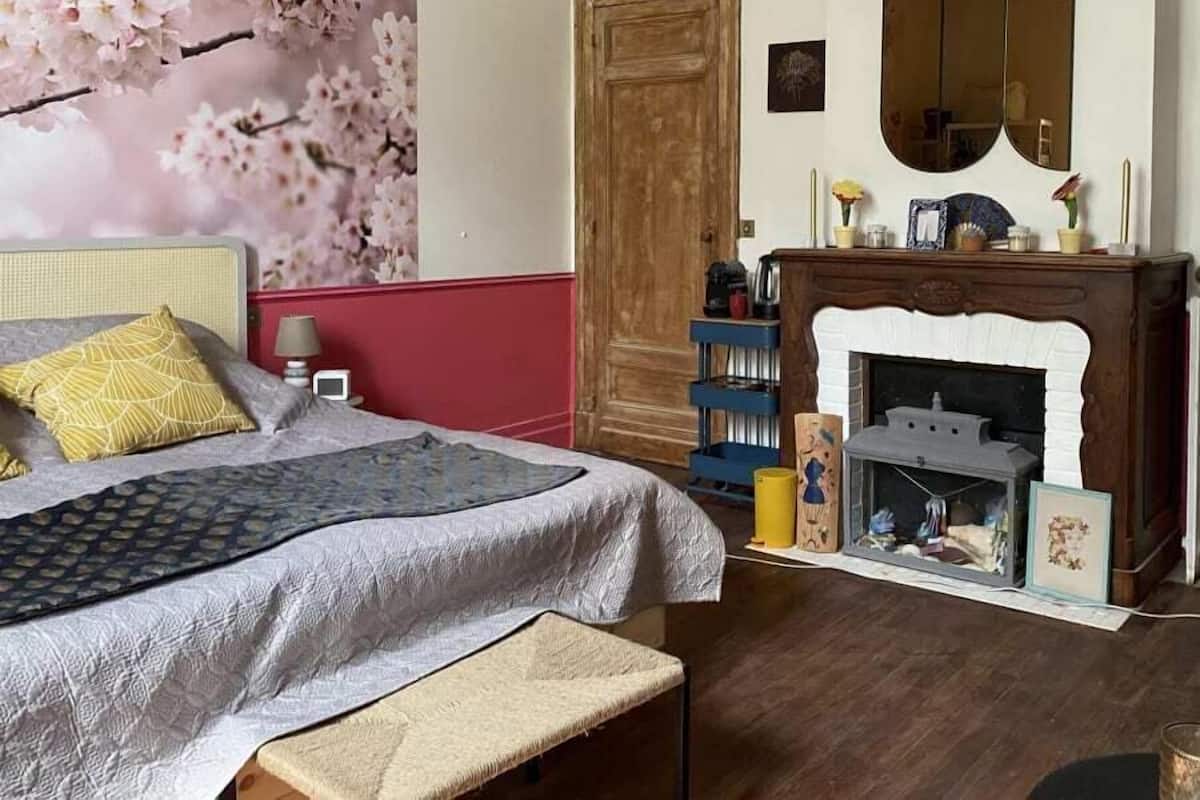 Ένα υπνοδωμάτιο με ένα κρεβάτι, έναν πάγκο, ένα τζάκι, έναν καθρέφτη και έναν τοίχο διακοσμημένο με ταπετσαρία με σχέδια ανθισμένων κερασιών.