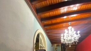 Un corridoio con una scala in legno, un lampadario e un cartello che indica la direzione dei bagni.