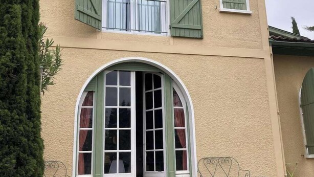 Un edificio a due piani con facciata beige, persiane verdi e un'ampia entrata ad arco.