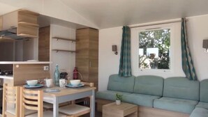 A compact living space with a kitchenette, a dining area, and a seating area with a sofa and a small table. - Annick Mobilhome (Vias)