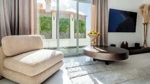 A modern living room with a beige sofa, a round coffee table, and a large window with a view of greenery and buildings. - New and Luxurious Villa Los Olivos  (Adeje)