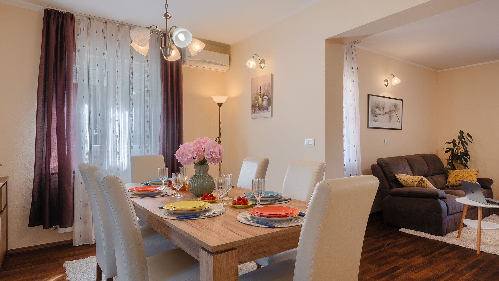 Un coin repas avec une table en bois dressée pour quatre personnes, entourée de chaises. On peut voir un vase rempli de fleurs sur la table, ainsi qu’un tableau accroché au mur.