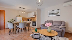 Un espace de vie compact comprenant un coin repas, une kitchenette et un canapé agrémenté d’un vase de fleurs.
