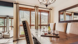 Un comedor con una mesa de madera, sillas y vistas a montañas a través de amplios ventanales.