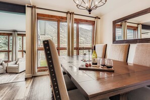 A dining area with a wooden table, chairs, and a view of mountains through large windows.