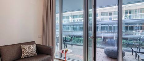 A modern living room with a sofa, a small round table, and a large sliding glass door leading to an outdoor deck.