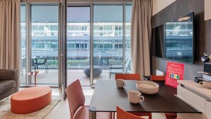 Habitación de hotel moderna con zona de comedor, ventanas amplias y vistas a la ciudad.