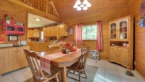 Interior de una cabaña de madera con una mesa de comedor, sillas y una zona de cocina.