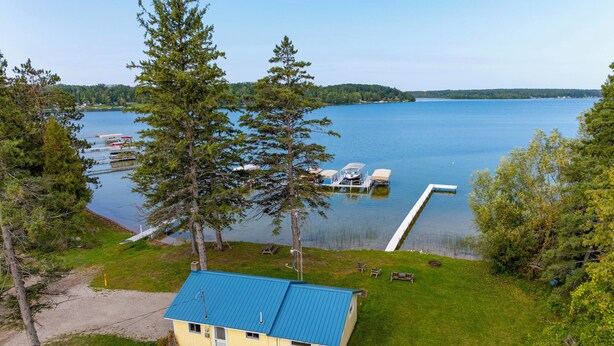 A lakeside cabin with a blue roof, dock, and dock chairs. - Mullett Lake Cabin w/ Private Dock & Fire Pit! (Indian River)