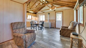 A spacious room with a high ceiling, wooden beams, a dining area with a table and chairs, and a cozy seating area with a cushioned chair and a small table. - Mullett Lake Cabin w/ Private Dock & Fire Pit! (Indian River)
