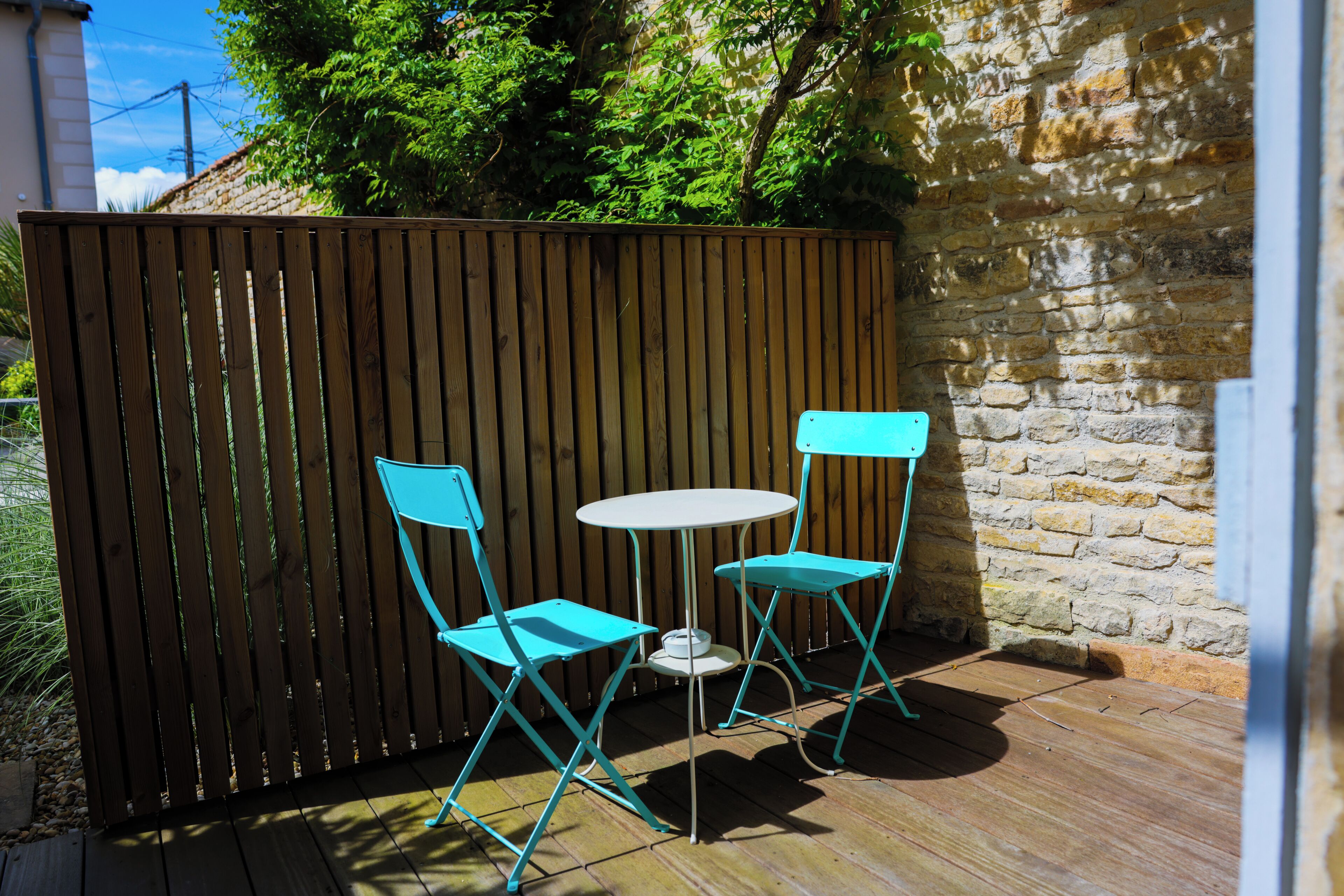 Een terras met een houten omheining, twee turquoise stoelen en een klein, rond tafeltje.