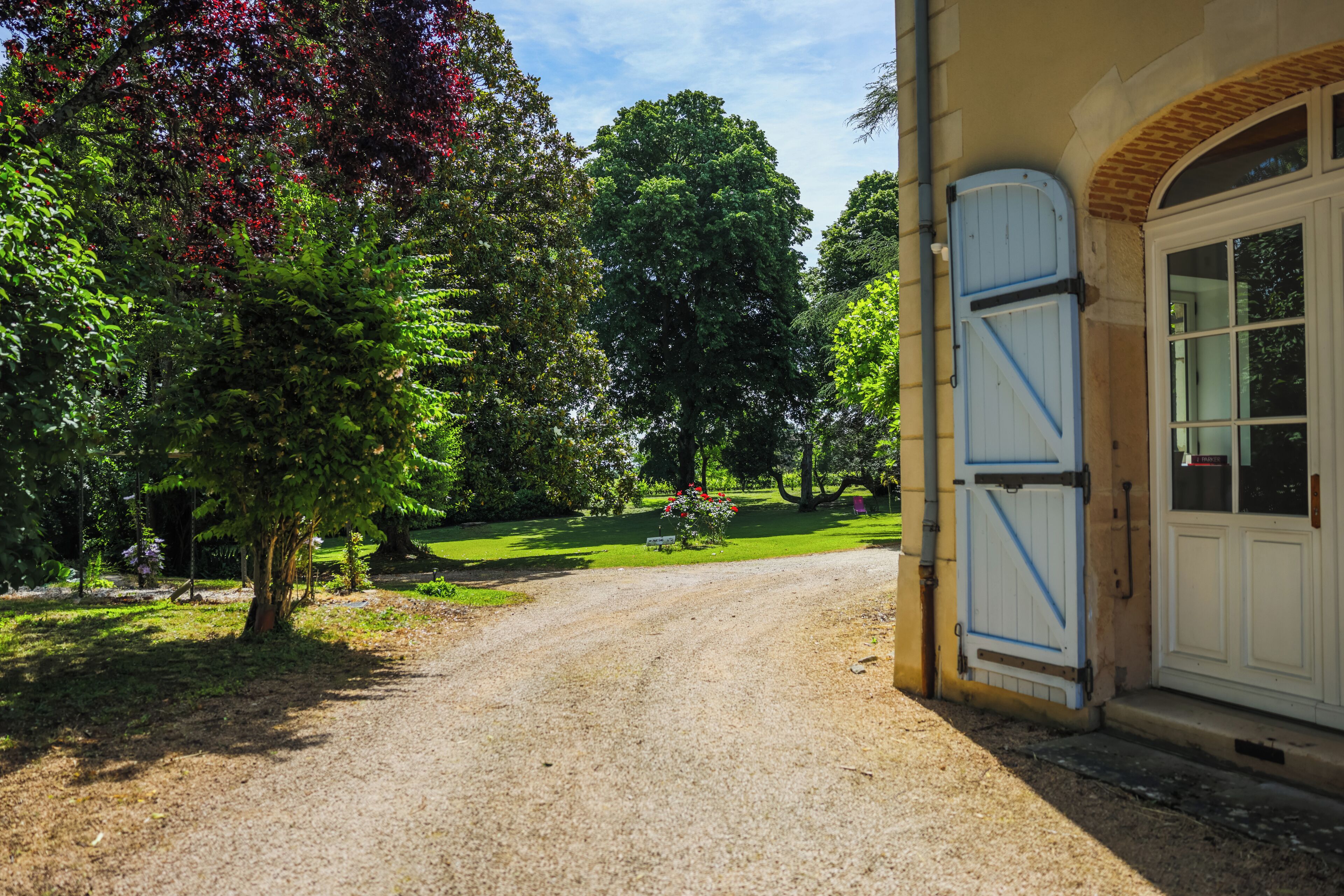 A gravel driveway leading to a building with a white door and blue shutters.