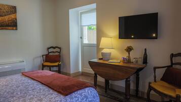 Habitación de hotel con cama, dos sillas, una mesa con lámpara, televisión y ventana con vista a zonas verdes.